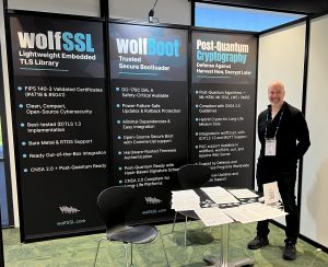 wolfSSL Lead Engineer Sean Parkinson standing in front of the wolfSSL, wolfBoot, and Post-Quantum Cryptography panels.